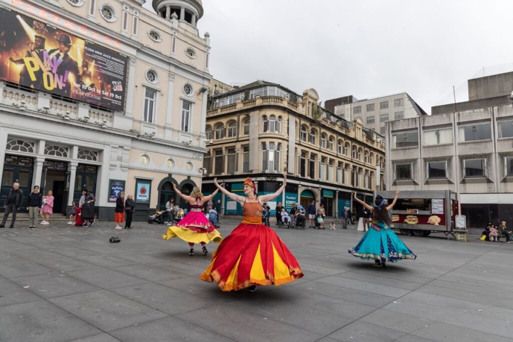 Street performers in colorful dresses dancing in a Liverpool square, showcasing cultural life in one of the Best Cities in the UK.