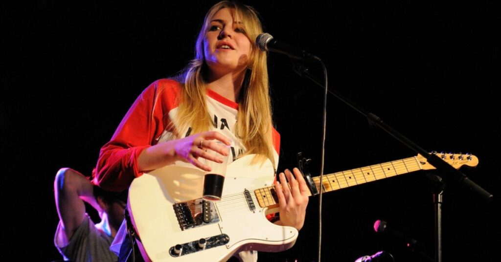 Rebecca Lucy Taylor performing live on stage with white guitar as Self Esteem, featured by The London Magazine